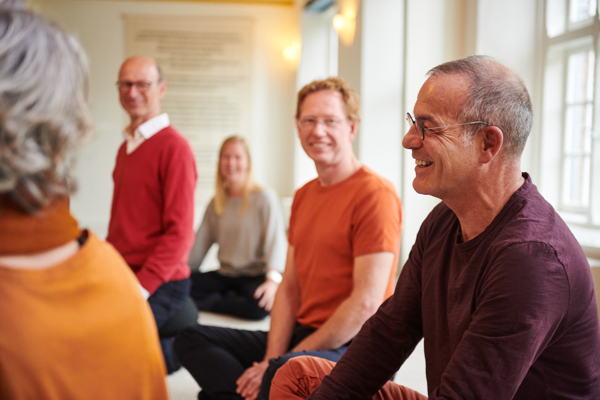 Groep deelnemers zit in een kring en lacht tijdens een bijeenkomst over gezonde zelfliefde bij de School voor Zijnsoriëntatie